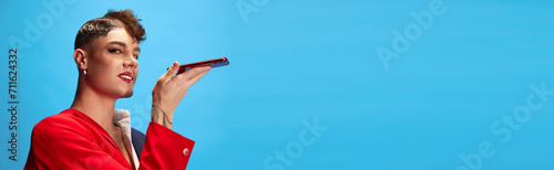 Banner. Male model with masculine and feminine appearance talking on phone against blue background with negative space to insert text. Concept of business, self-expression, delivery, connection. Ad photo