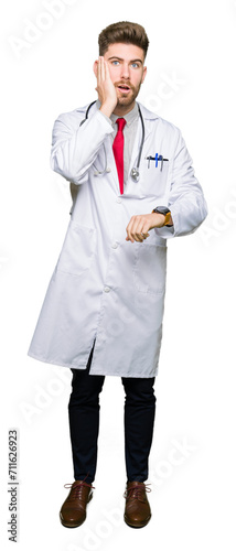 Young handsome doctor man wearing medical coat Looking at the watch time worried, afraid of getting late