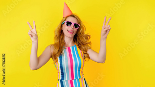 Dancing excited fashionable woman, tongue out, having fun enjoying rhythm to music, entertainment. Carefree playful smiling lady, trend makeup, colorful outfit for ad, fashion, party. Studio on yellow