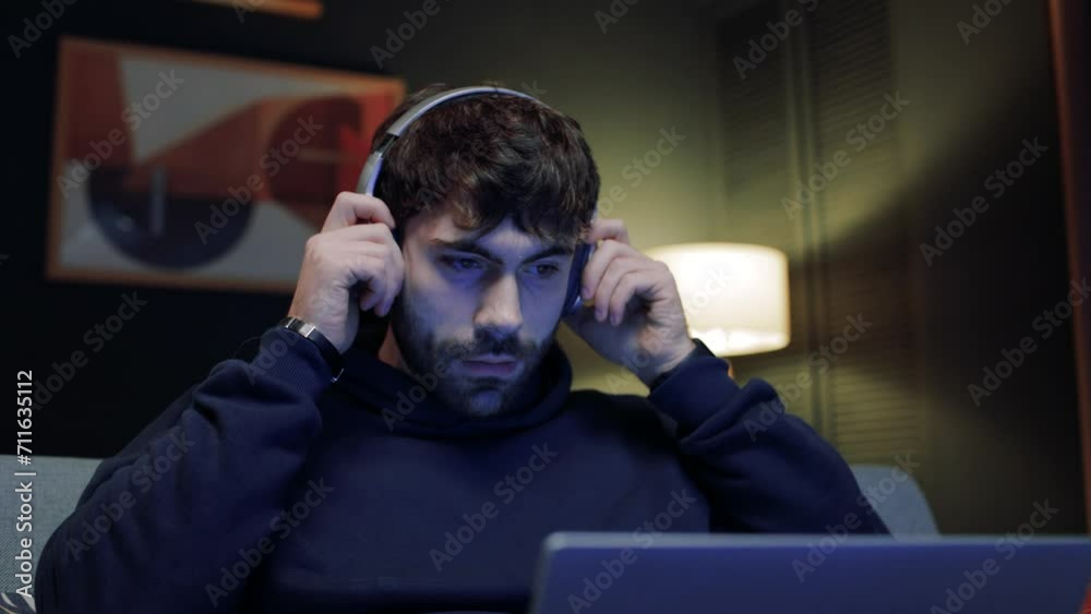 Portrait of male holding laptop. Bearded man trying headphones on. Man using wireless headphones. Man sitting at couch and enjoying music. Male relax at modern flat. Man listening songs. Portrait of male holding laptop. Bearded man trying headphones on. Man using wireless headphones. Man sitting at couch and enjoying music. Male relax at modern flat. Man listening songs.