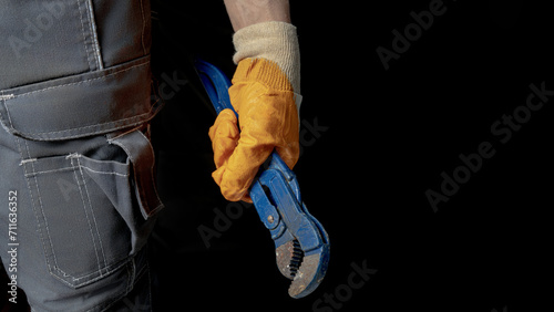 A man's hand holds an adjustable wrench on a black background. Place to place text.