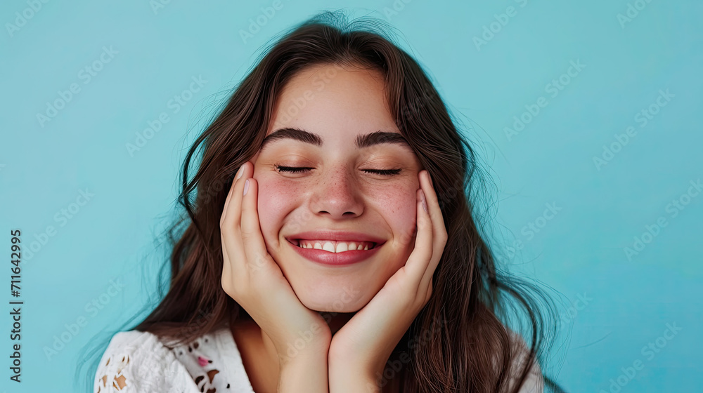 Cheerful female smiling for camera and clasping hands under cheek while pretending to sleep against blue background Cheerful female smiling for camera and clasping hands under cheek while pretending to sleep against blue background