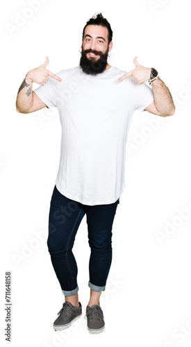 Young hipster man with long hair and beard wearing casual white t-shirt looking confident with smile on face, pointing oneself with fingers proud and happy. © Krakenimages.com