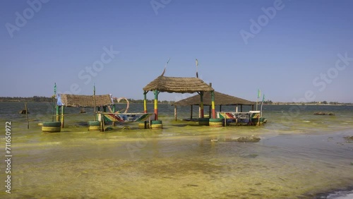 Pan right of thatched shelter on stilts on the shores of Lake Retba, Senegal. Lake Retba, also known as Lac Rose, is renowned for its vivid pink waters caused by Dunaliella salina algae. 4K UHD video. photo