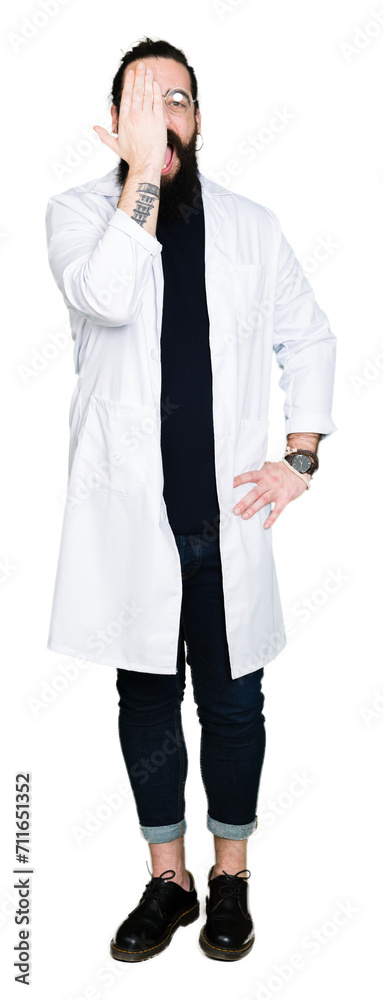 Doctor therapist man with long hair and bear wearing white coat covering one eye with hand with confident smile on face and surprise emotion. Doctor therapist man with long hair and bear wearing white coat covering one eye with hand with confident smile on face and surprise emotion.
