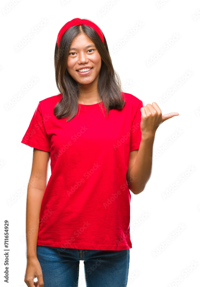 Young asian woman over isolated background smiling with happy face looking and pointing to the side with thumb up. Young asian woman over isolated background smiling with happy face looking and pointing to the side with thumb up.