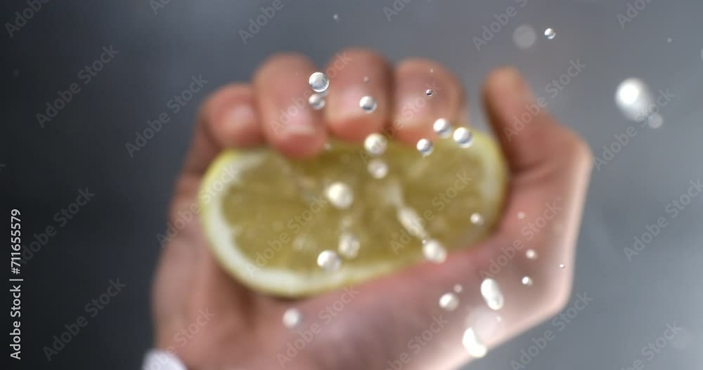 Super slow motion of professional bartender is squeezing fresh slice of lemon fruit while preparing an alcoholic cocktail with ice cubes to customers at the bar or disco club at 1000fps.
