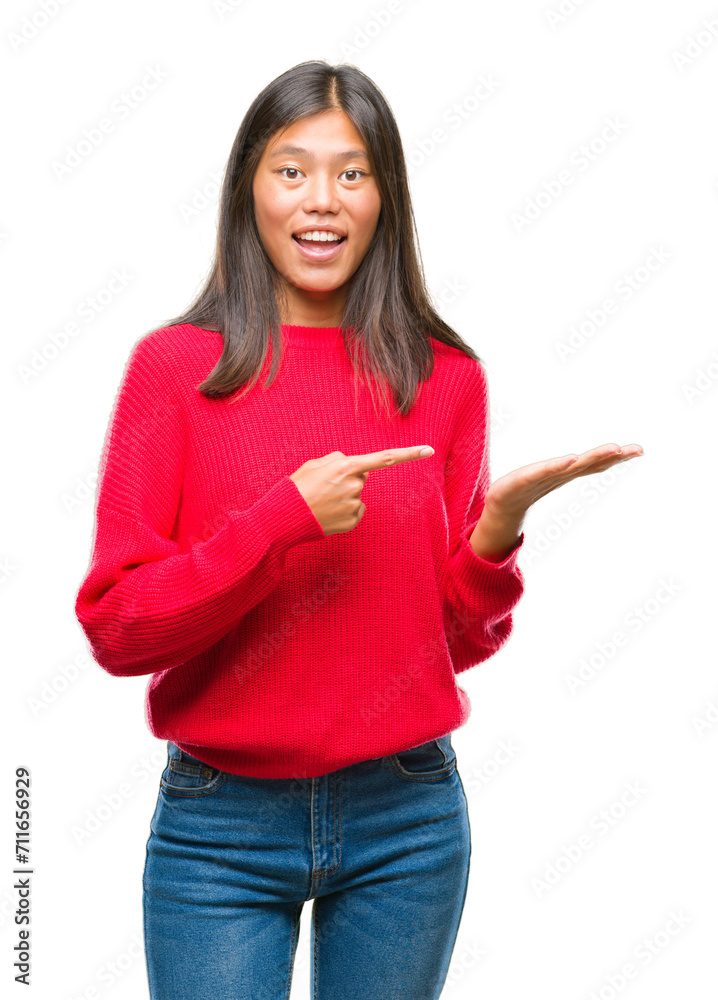 Young asian woman wearing winter sweater over isolated background amazed and smiling to the camera while presenting with hand and pointing with finger.