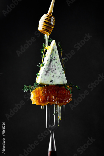 Blue cheese with honey on a fork. Honeycombs. On a black background. Creative photo.