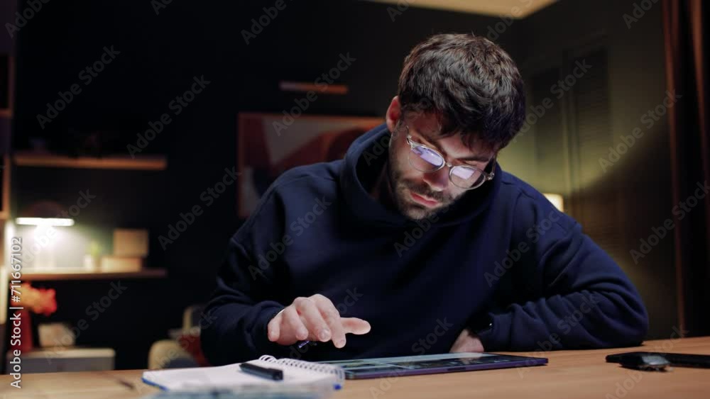 Portrait of man in glasses using tablet. Male sitting at table and working with gadget. Serious man touching screen of device. Man working freelancing at home. Concentrated man browsing in Internet. Portrait of man in glasses using tablet. Male sitting at table and working with gadget. Serious man touching screen of device. Man working freelancing at home. Concentrated man browsing in Internet.