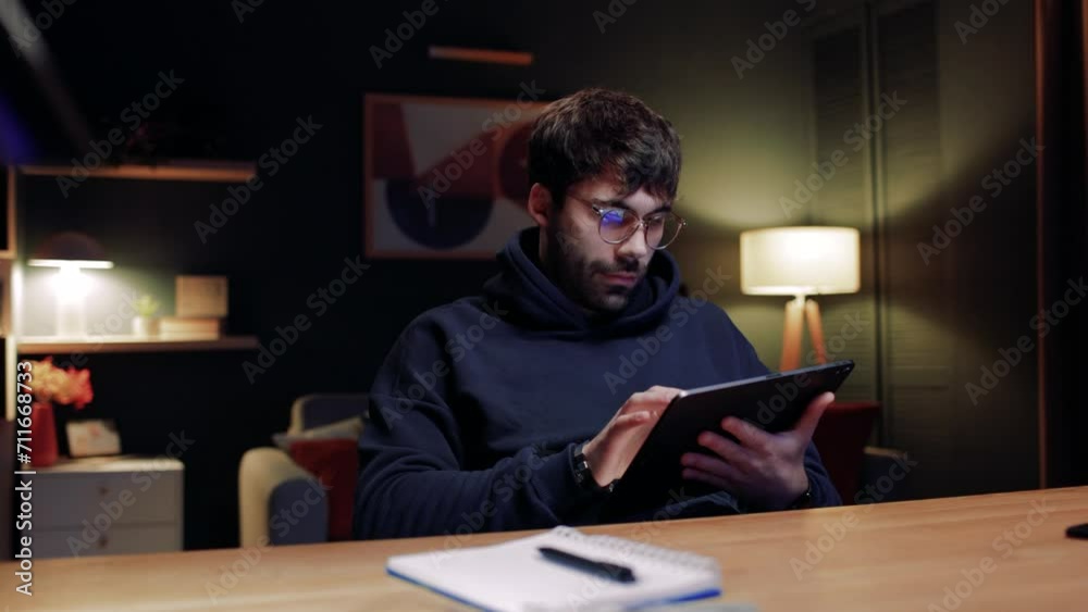 Man relaxing at home. Male wearing glasses and using tablet. Man holding tablet and watching funny videos. Male smiling sitting at table. Man chilling at well designed home. Man relaxing at home. Male wearing glasses and using tablet. Man holding tablet and watching funny videos. Male smiling sitting at table. Man chilling at well designed home.