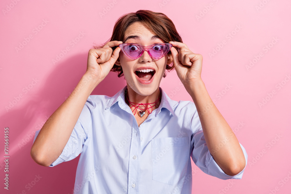 Portrait of positive astonished lady hands touch sunglass open mouth isolated on pink color background Portrait of positive astonished lady hands touch sunglass open mouth isolated on pink color background