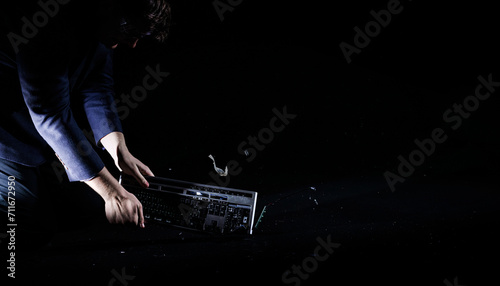 Businessman hard banging a computer keyboard on a concrete floor, destroying it to small pieces, slow motion shot. Overwork and job burnout concepts. photo