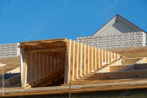 A new wooden roof structure lining a house in the city. Industrial roofing system with wooden beams, ceilings and tiles. Roofing works.