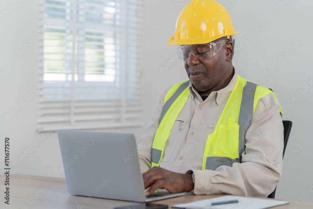 Professional of man architect industrial engineer Standing in the office, foreman in helmet using laptop working with new construction project architectural plan. Professional of man architect industrial engineer Standing in the office, foreman in helmet using laptop working with new construction project architectural plan.