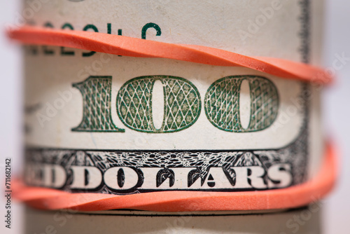 Close-up of a US one hundred dollar bill in a roll with a bank elastic band.