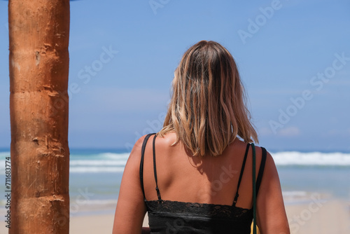 Woman stands with her back on the beach in front of the ocean