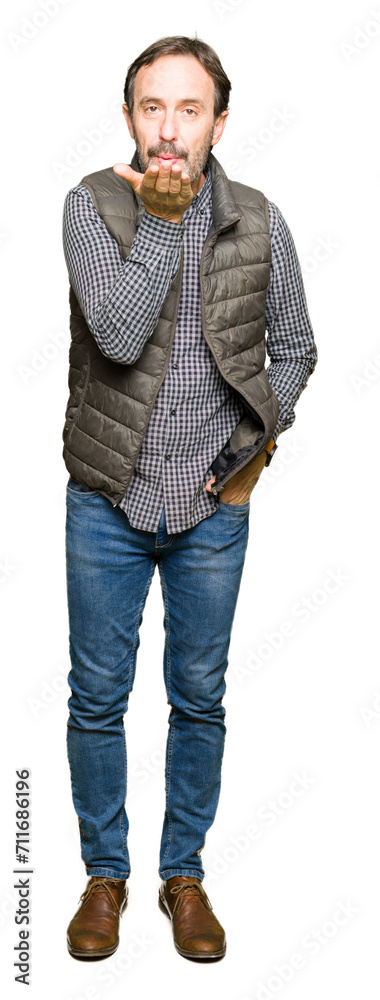 Middle age handsome man wearing winter vest looking at the camera blowing a kiss with hand on air being lovely and sexy. Love expression. Middle age handsome man wearing winter vest looking at the camera blowing a kiss with hand on air being lovely and sexy. Love expression.