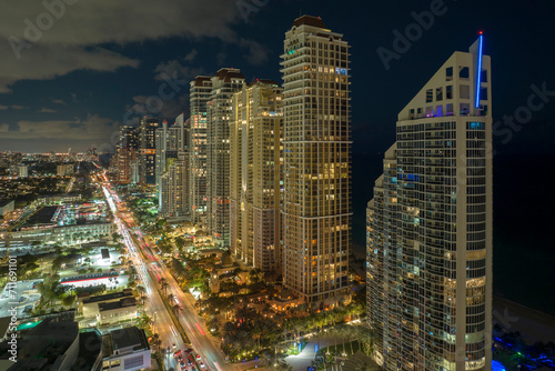 View from above of brightly illuminated city street with dense traffic and high skyscraper buildings in downtown of Sunny Isles Beach in Florida, USA. American tourist urban district at night