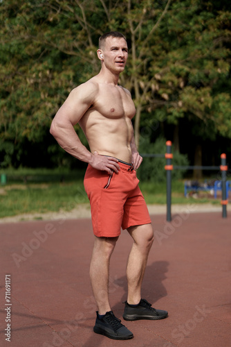 A fit male athlete stands confidently, hands on hips, after a successful outdoor workout, embodying strength and achievement
