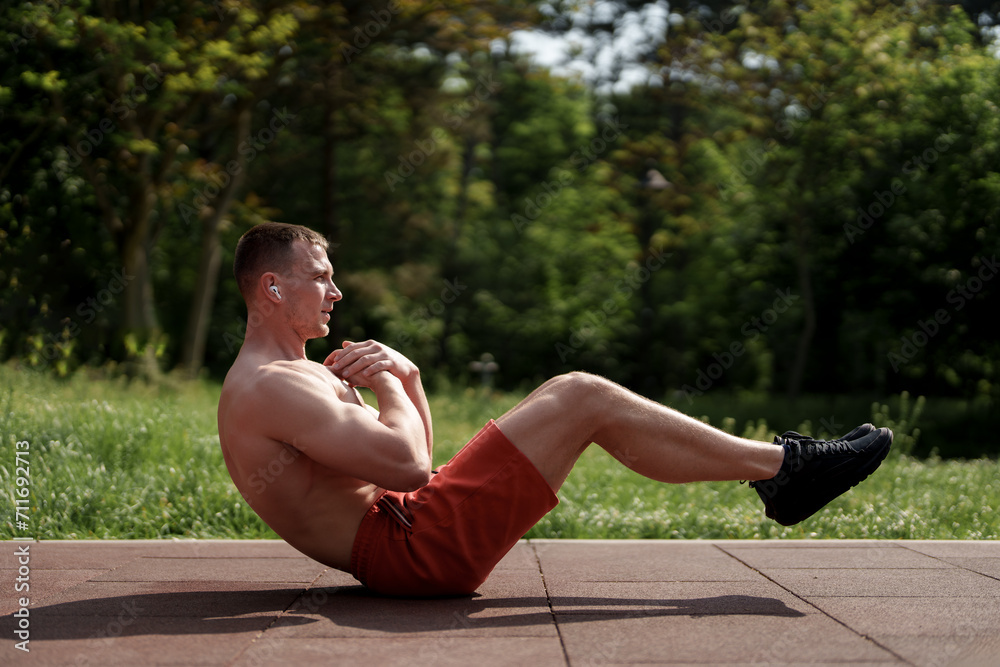 Fototapeta premium Focused man engaged in an abdominal workout in a serene park setting, emphasizing core strength