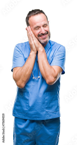 Middle age hoary senior doctor man wearing medical uniform over isolated background sleeping tired dreaming and posing with hands together while smiling with closed eyes.