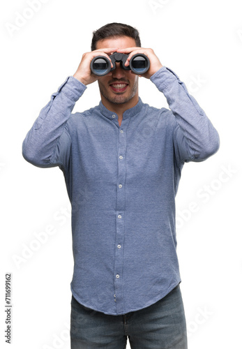 Handsome young man looking through binoculars with a happy face standing and smiling with a confident smile showing teeth