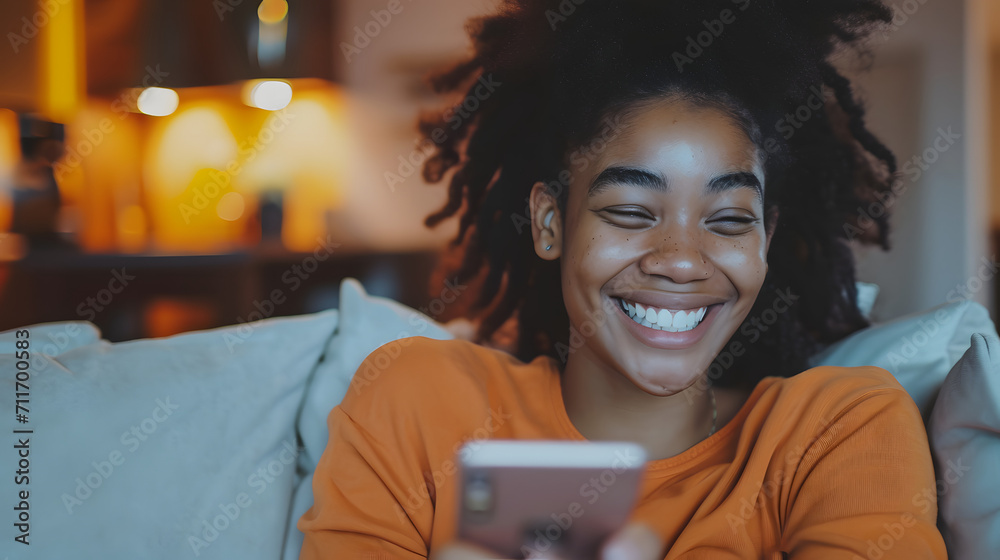 Naklejka premium Smiling young beauty black curly woman at home relaxed texting using mobile phone, technology communication concept
