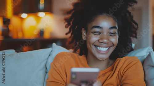 Smiling young beauty black curly woman at home relaxed texting using mobile phone, technology communication concept photo