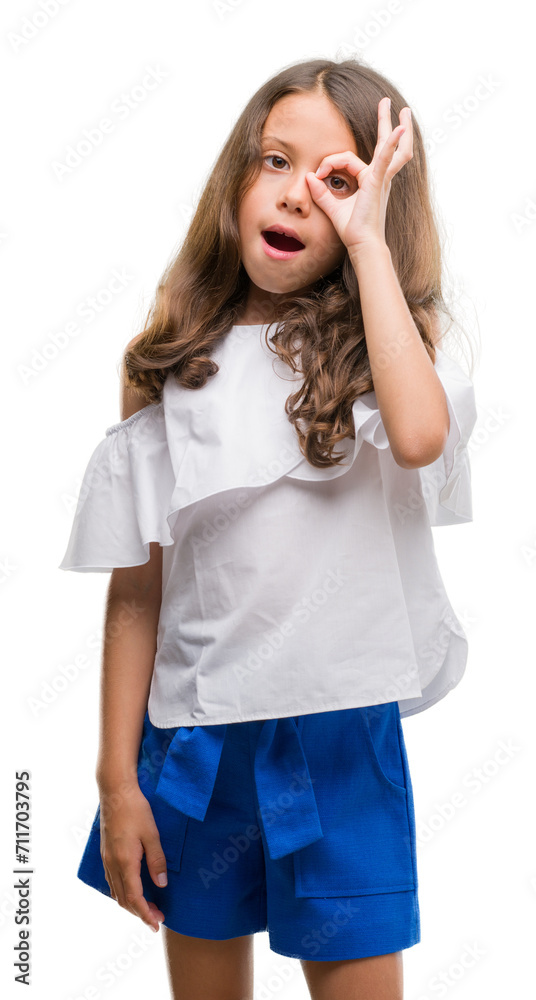 Brunette hispanic girl doing ok gesture shocked with surprised face, eye looking through fingers. Unbelieving expression. Brunette hispanic girl doing ok gesture shocked with surprised face, eye looking through fingers. Unbelieving expression.