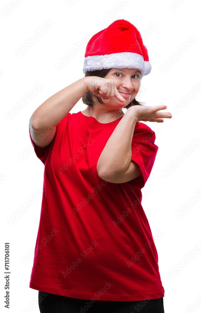Young adult woman with down syndrome wearing christmas hat over isolated background amazed and smiling to the camera while presenting with hand and pointing with finger. Young adult woman with down syndrome wearing christmas hat over isolated background amazed and smiling to the camera while presenting with hand and pointing with finger.