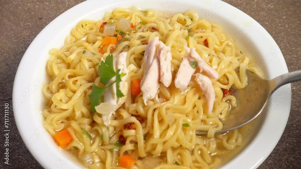 chicken soup with asian noodles and vegetables in white plate is scooped up with a spoon chicken soup with asian noodles and vegetables in white plate is scooped up with a spoon