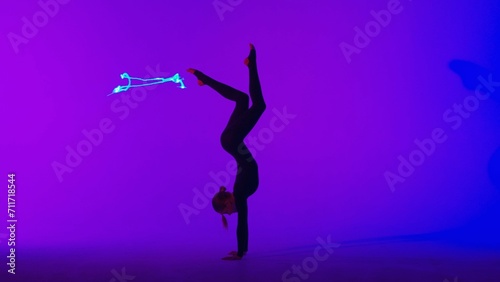 Female gymnast isolated on laser blue neon studio background. Girl dancer showing gymnastic elements on the floor.
