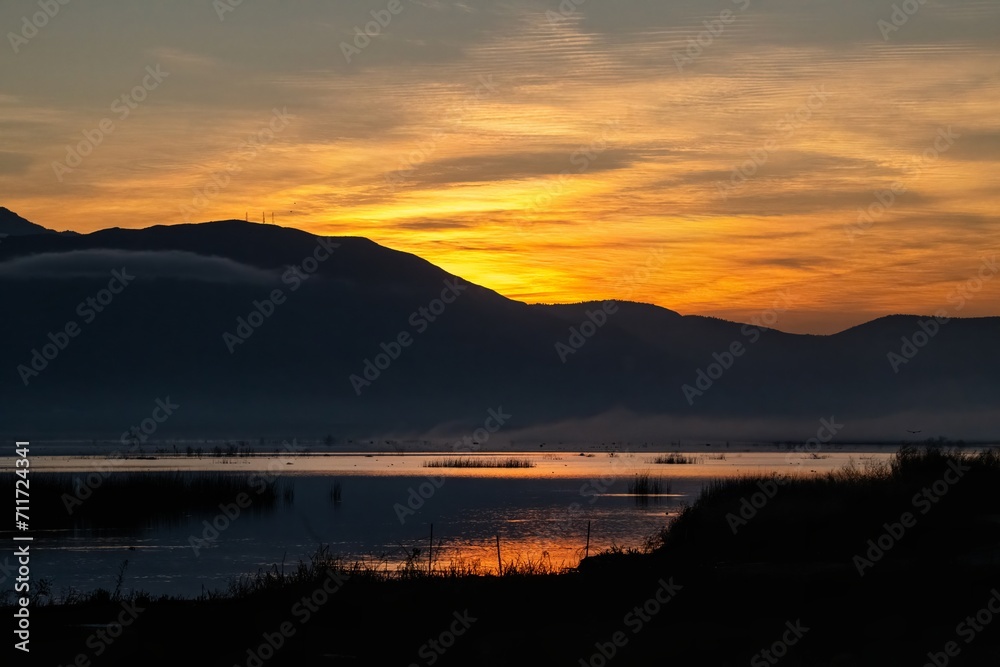 Obraz premium Sunrise golden hour over a lake with reflections and hills
