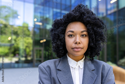 Portrait of a serious African American female student standing outside campus wearing a suit and looking confidently at the camera. Close-up photo.