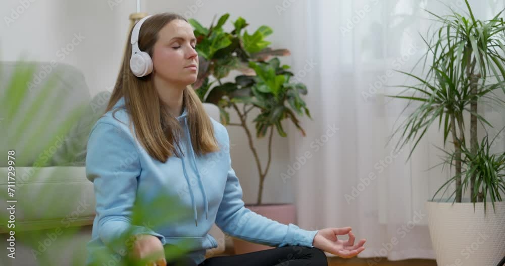 A happy young woman wearing headphones practicing yoga and meditation at home A happy young woman wearing headphones practicing yoga and meditation at home