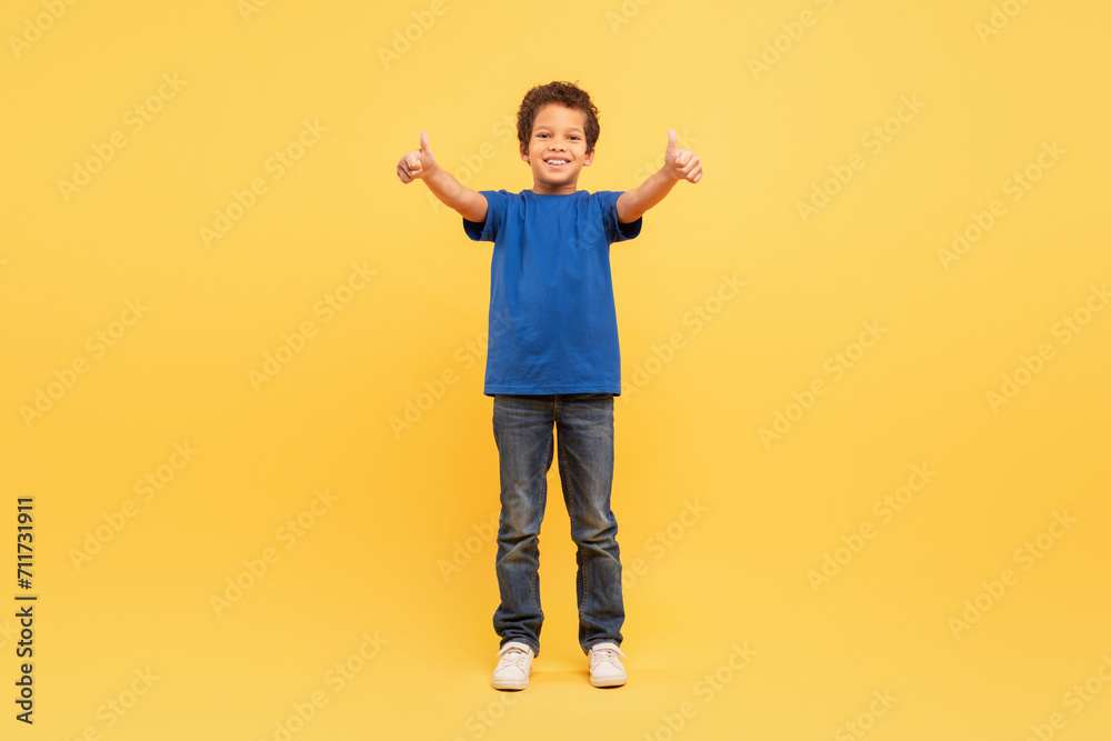 Cheerful boy giving thumbs up in blue shirt on yellow background Cheerful boy giving thumbs up in blue shirt on yellow background