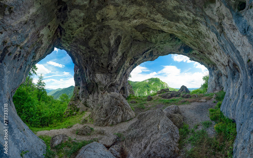 Viewpoint above mountains through a grotto, eroded in a calcareous cliff on a mountain side. The tunnel has its stone walls covered with moss. The arches in the cave resemble two eyes. Carpathia