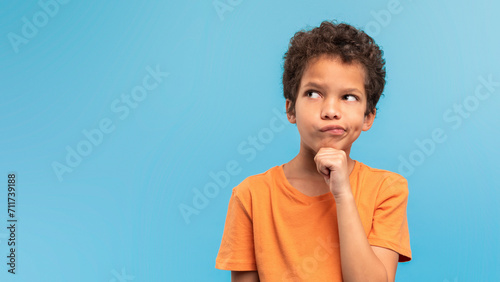 Quadro em tela Thoughtful boy in orange, pondering on blue background, free space