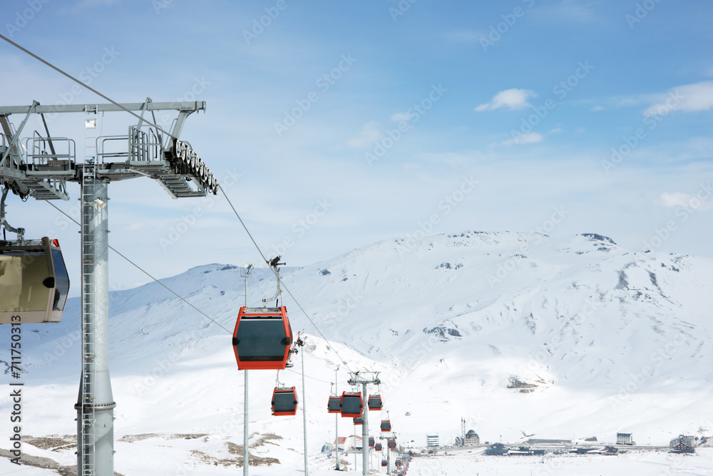 Cable car or ski lift cabins moving against the background of snow-covered mountains and blue sky in the mountain ski resort. Perspective. Winter, Vacation. Extreme sport. Travel content Cable car or ski lift cabins moving against the background of snow-covered mountains and blue sky in the mountain ski resort. Perspective. Winter, Vacation. Extreme sport. Travel content
