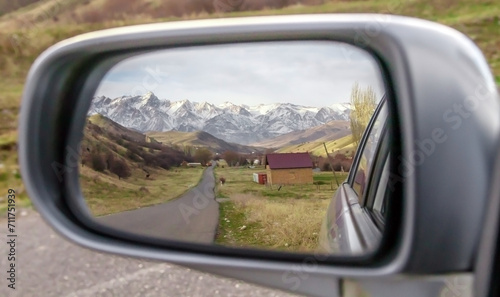 Reflection in the mirror of a car of beautiful snow-capped mountains and roads