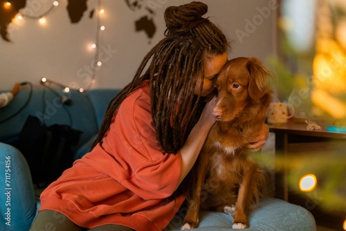 Young woman dreadlocks hugging dog toller at home on holidays, cute pets concept