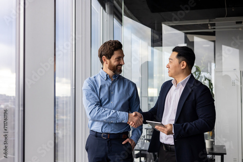Two professional businessmen shaking hands in a modern office, symbolizing partnership, collaboration, and successful business agreement.