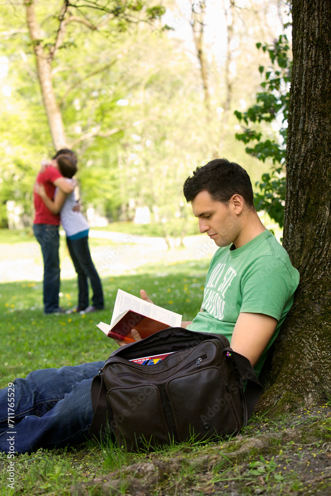 Young student learning in a park, young couple hugging in the background. Young student learning in a park, young couple hugging in the background.