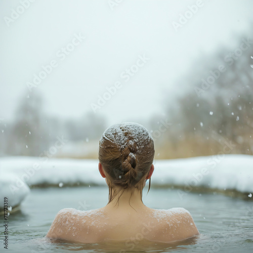 Rear back view of a woman's winter swim in ice hole of a frozen lake with snow and copy space