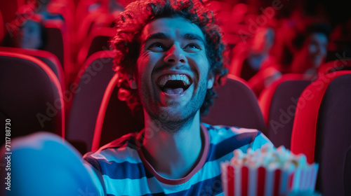 Young man with popcorn watching with interest a movie in the cinema and laughing.