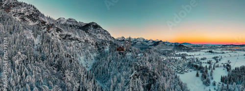 A breathtaking winter panorama of Neuschwanstein Castle, the fairy-tale palace of King Ludwig II of Bavaria, nestled among the snow-covered Alps and forests.