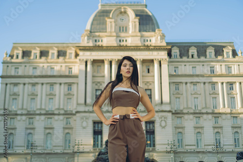 young Latin woman looks confidently at camera with her back to Kirchner cultural center, old palace photo