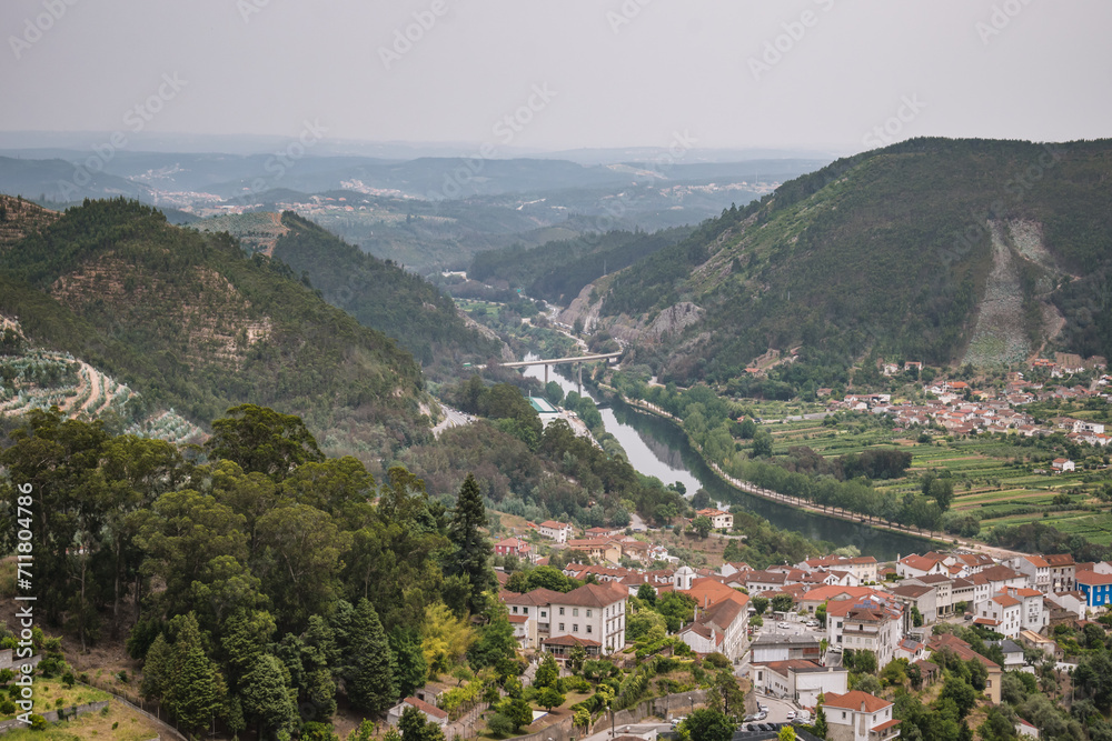 Aerial view of Mondego river in valley and architecture of Penacova village with gradient mountains in horizon, PORTUGAL