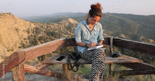 Young woman sitting on bench writing in notebook at Vashlovani national park in Georgia photo